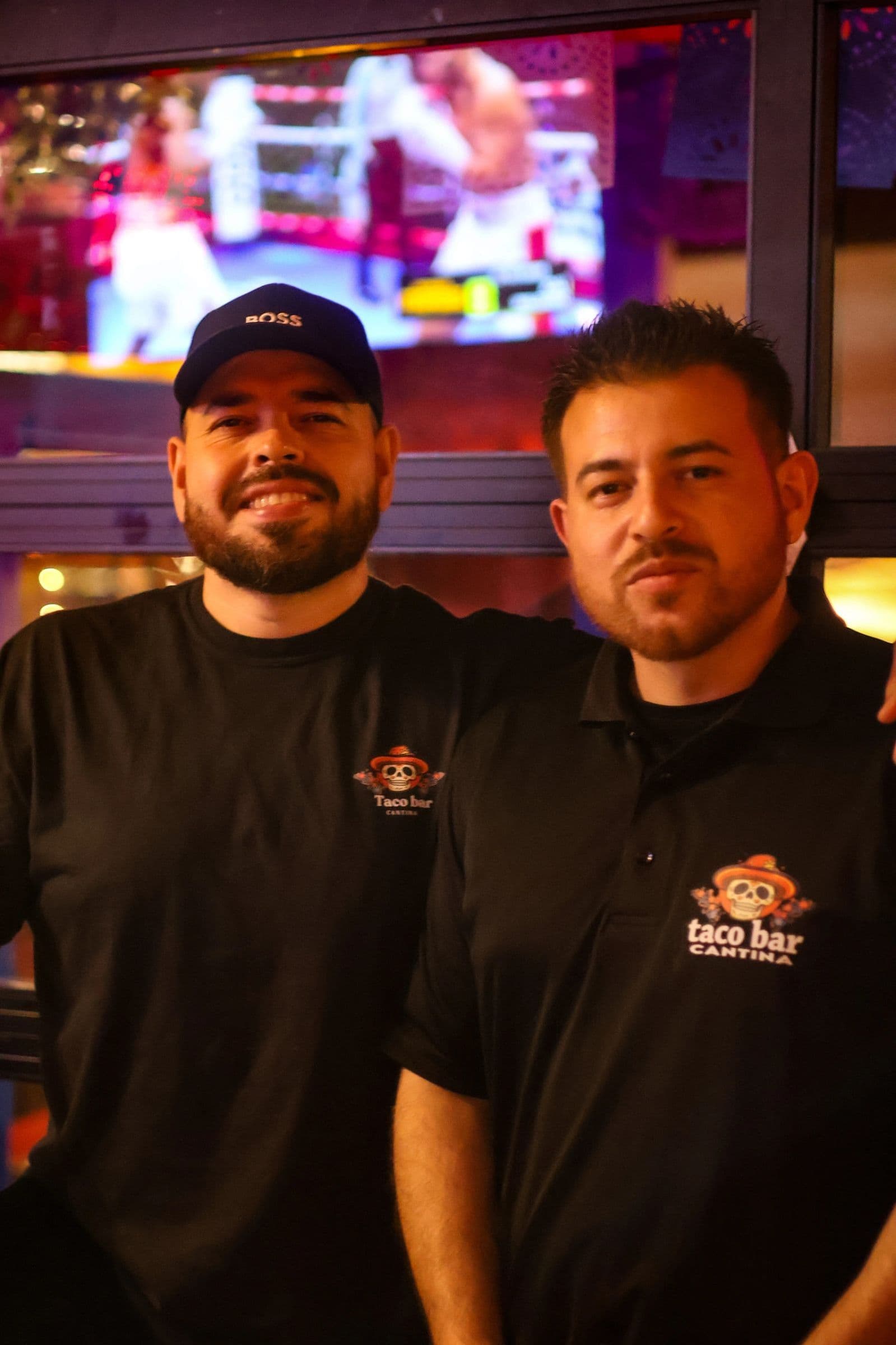 The two owners of Taco Bar Cantina in branded shirts inside the restaurant